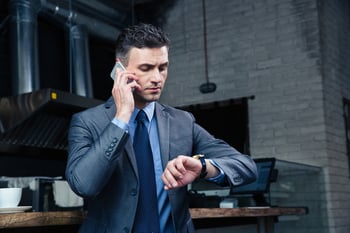 Confident businessman speaking on the phone and looking on the wristwatch in cafe